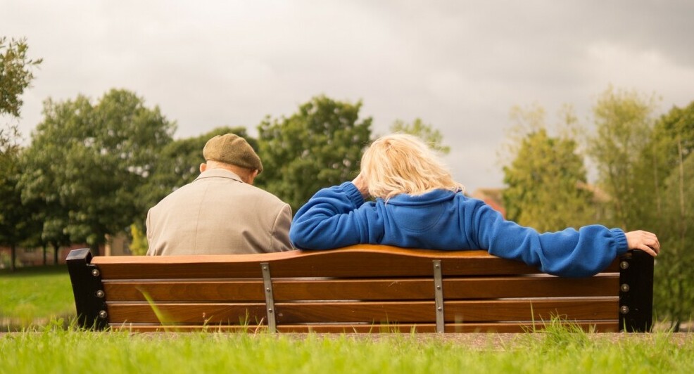 back view of older couple sitting on bench in nature